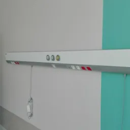 Świeżo pomalowana ściana w szpitalu z poziomą listwą z gniazdkami i przyciskami, pomalowana na szaro i turkusowo.