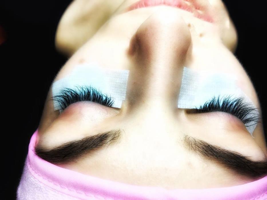 Zbliżenie na twarz kobiety z aplikowanymi sztucznymi rzęsami; widoczne plasterki ochronne pod oczami i różowa opaska na włosach.