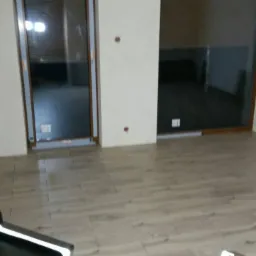 Ułożone panele podłogowe imitujące drewno w jasnym odcieniu, widoczne fragmenty ścian z widocznymi otworami po gniazdkach i ościeżnicami okiennymi.