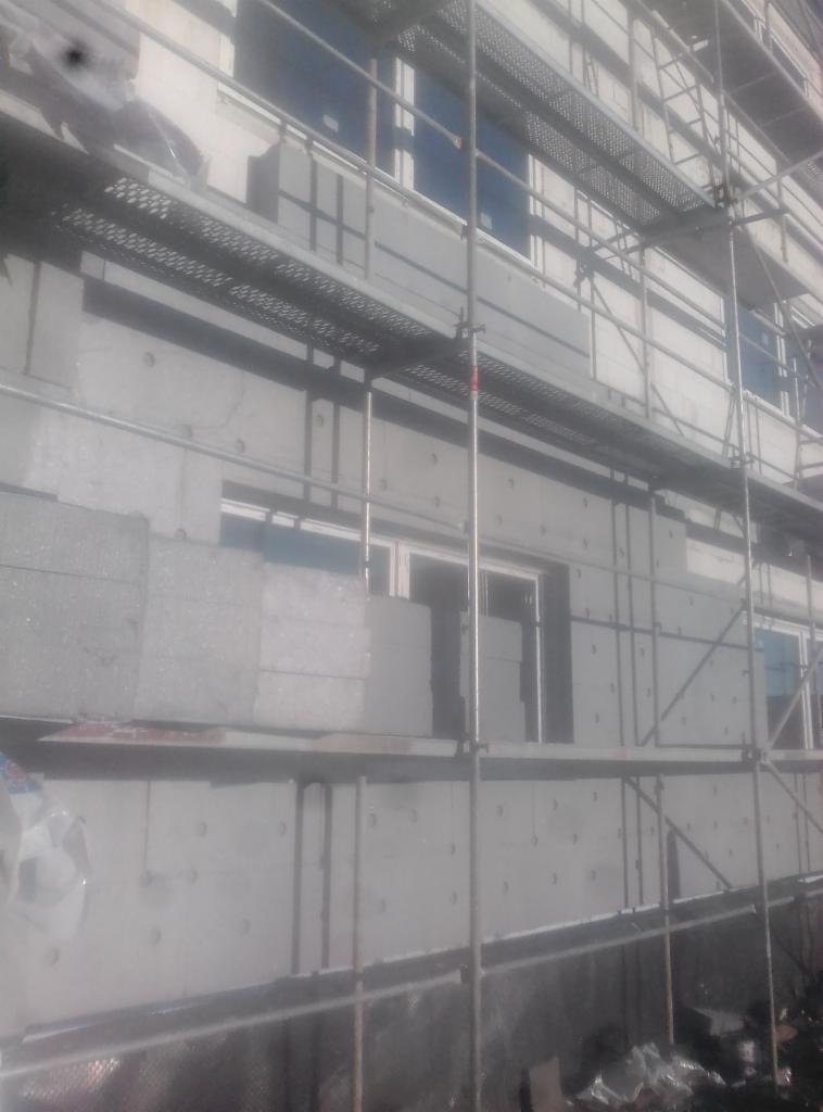 Ocieplanie elewacji budynku wielorodzinnego z widocznymi rusztowaniami i częściowo zamontowanymi płytami izolacyjnymi.