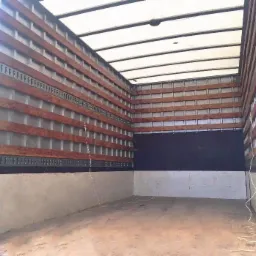 Wnętrze pustej przestrzeni ładunkowej busa z drewnianymi listwami mocującymi i metalowymi szynami, widok od tyłu pojazdu.