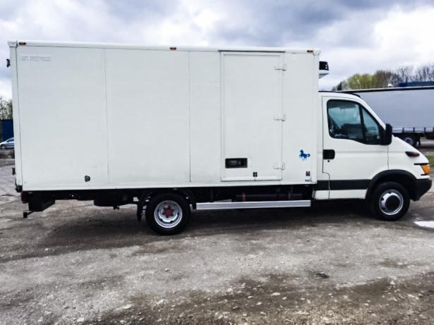 Biały samochód dostawczy typu chłodnia z niebieskim logo konika na boku, zaparkowany na szarym betonowym placu.