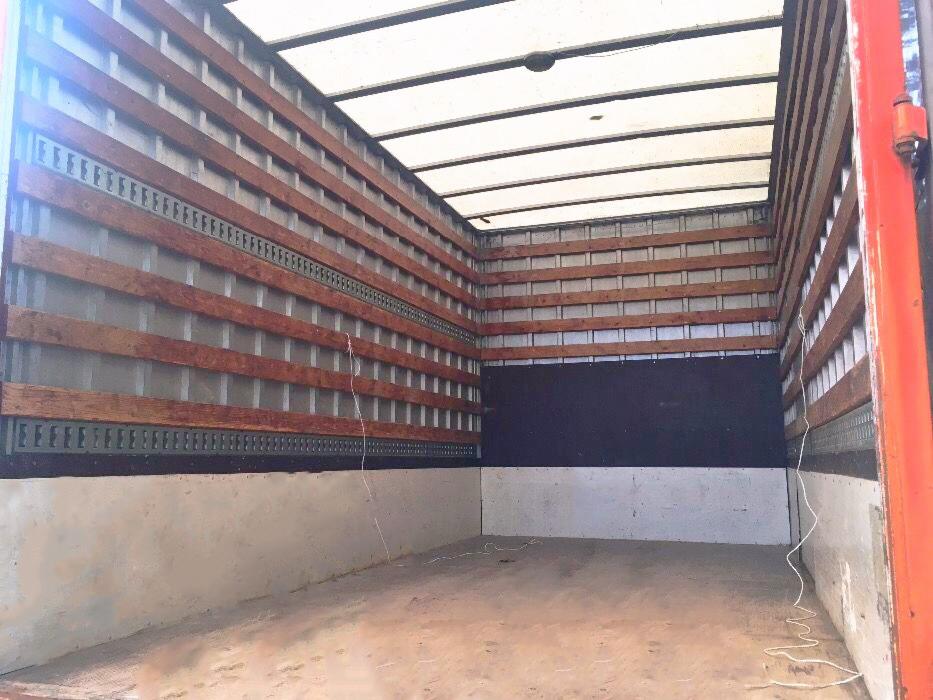 Wnętrze pustej przestrzeni ładunkowej busa z drewnianymi listwami mocującymi i metalowymi szynami, widok od tyłu pojazdu.