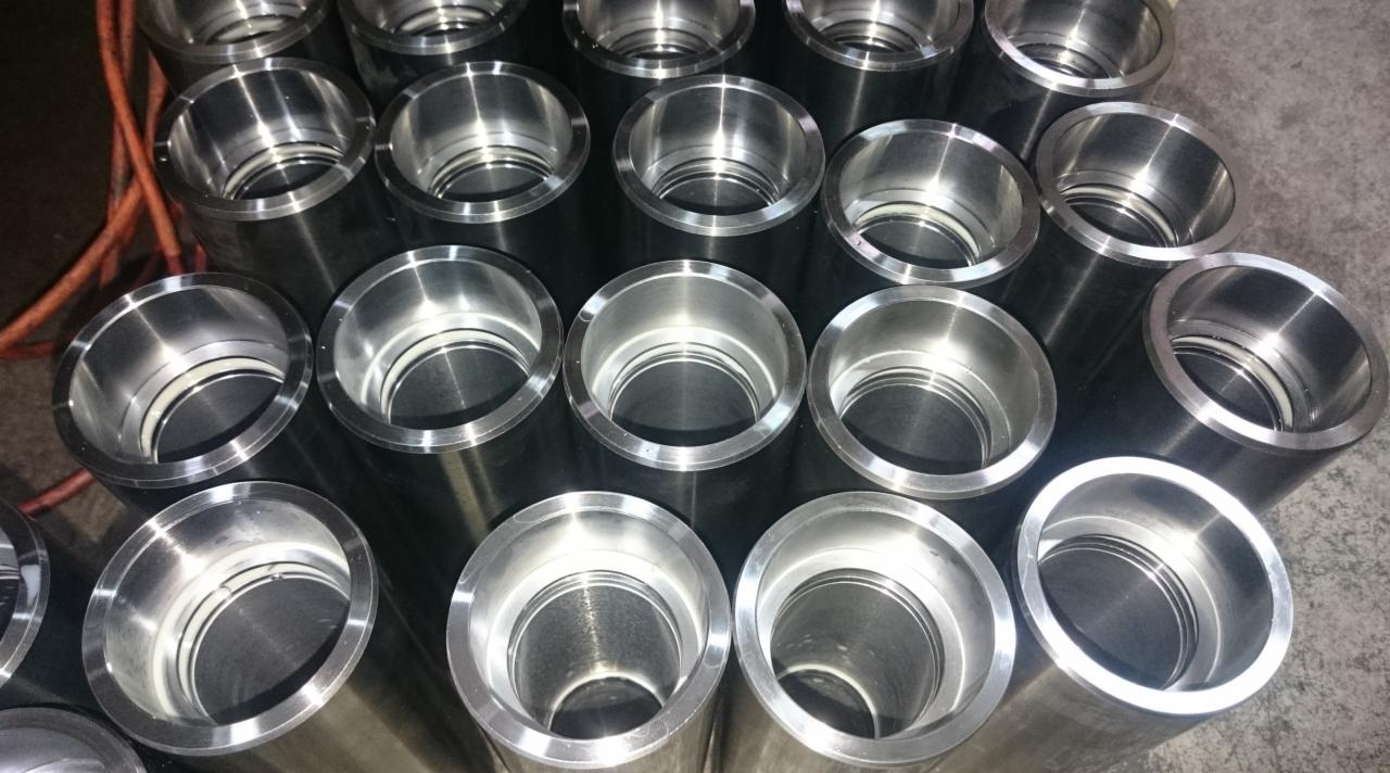 Grupowe ujęcie precyzyjnie obrobionych, metalowych tulei o gładkich, srebrzystych powierzchniach wewnętrznych i zewnętrznych, ułożonych blisko siebie na szarym tle.