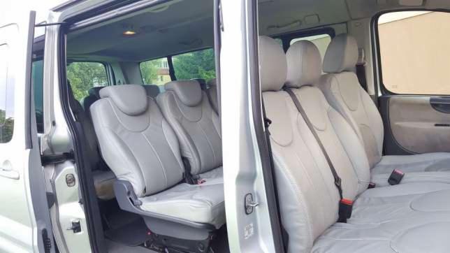 Wnętrze busa z trzema rzędami jasnoszarych skórzanych siedzeń, widok z otwartych drzwi bocznych.