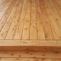 Świeżo położony, drewniany taras z widocznymi schodami, delikatnie mokry od wody, z oknem w tle.