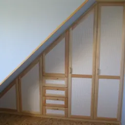 Drewniana szafa wnękowa na poddaszu ze wzorem plecionki na frontach, dopasowana do skosu dachu.