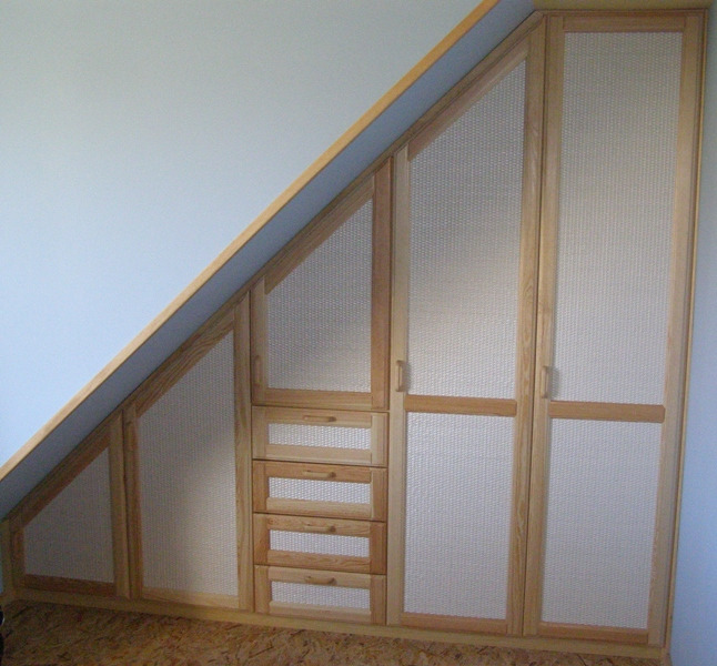 Drewniana szafa wnękowa na poddaszu ze wzorem plecionki na frontach, dopasowana do skosu dachu.