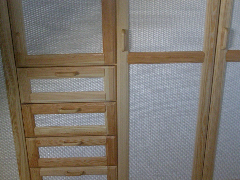 Drewniana szafa na wymiar z jasnymi, plecionymi wypełnieniami frontów szuflad i drzwi, widoczne słoje drewna.