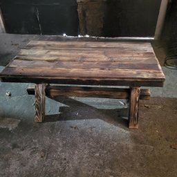 Sewostyle Meble na wymiar altanki spawanie - Rustykalny stolik kawowy z ciemnego drewna, wykonany ręcznie. Widoczne słoje i naturalne niedoskonałości drewna. Surowy styl, idealny do wnętrz w stylu loft.