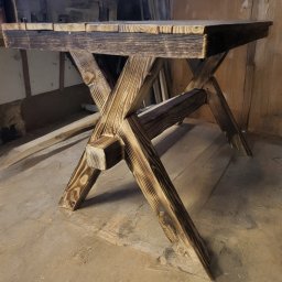 Sewostyle Meble na wymiar altanki spawanie - Drewniany stół z blatem z desek i nogami w kształcie litery X, wykonany w stylu rustykalnym z widoczną strukturą drewna i efektem opalania.