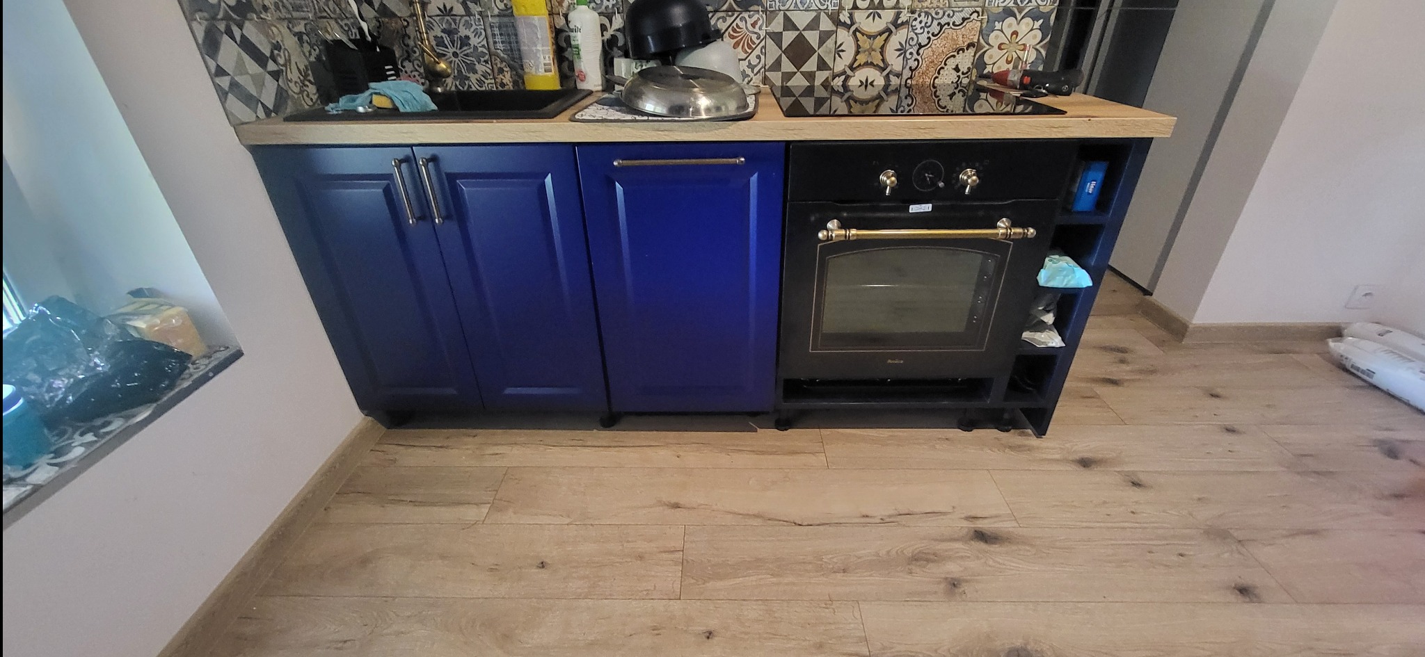 Niebieskie szafki kuchenne z drewnianym blatem i czarnym piekarnikiem w stylu retro, nad którymi widać wzorzyste płytki.