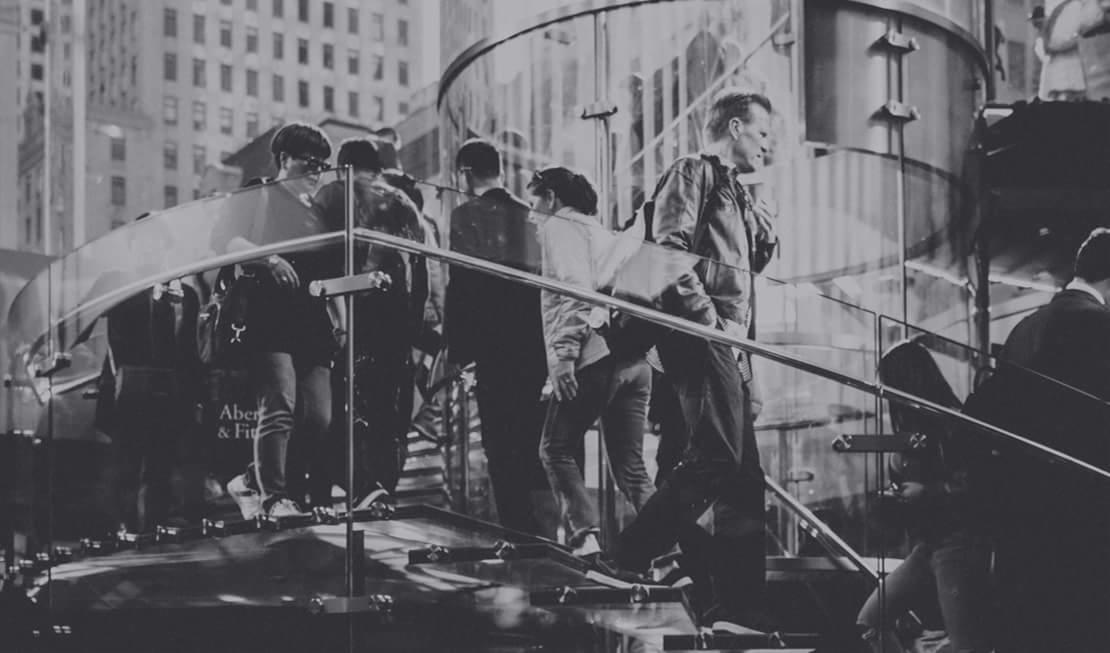 Czarno-białe zdjęcie grupy osób w Rzeszowie wchodzących po schodach z przezroczystymi barierkami, w tle budynki miejskie.