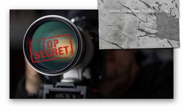 Obiektyw kamery z nałożoną czerwoną pieczęcią 'TOP SECRET', w tle fragment szarej tekstury z adresem strony internetowej.