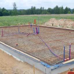 Zbrojona płyta fundamentowa z wyprowadzonymi instalacjami wodno-kanalizacyjnymi na tle zieleni