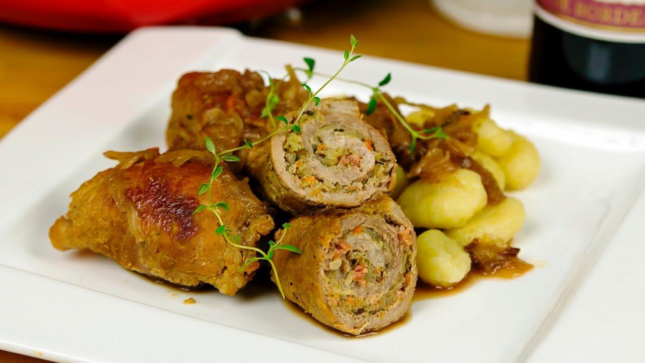 Rolada mięsna przekrojona na pół, faszerowana warzywami, podana z kluskami i sosem cebulowym, udekorowana gałązkami tymianku na białym talerzu.