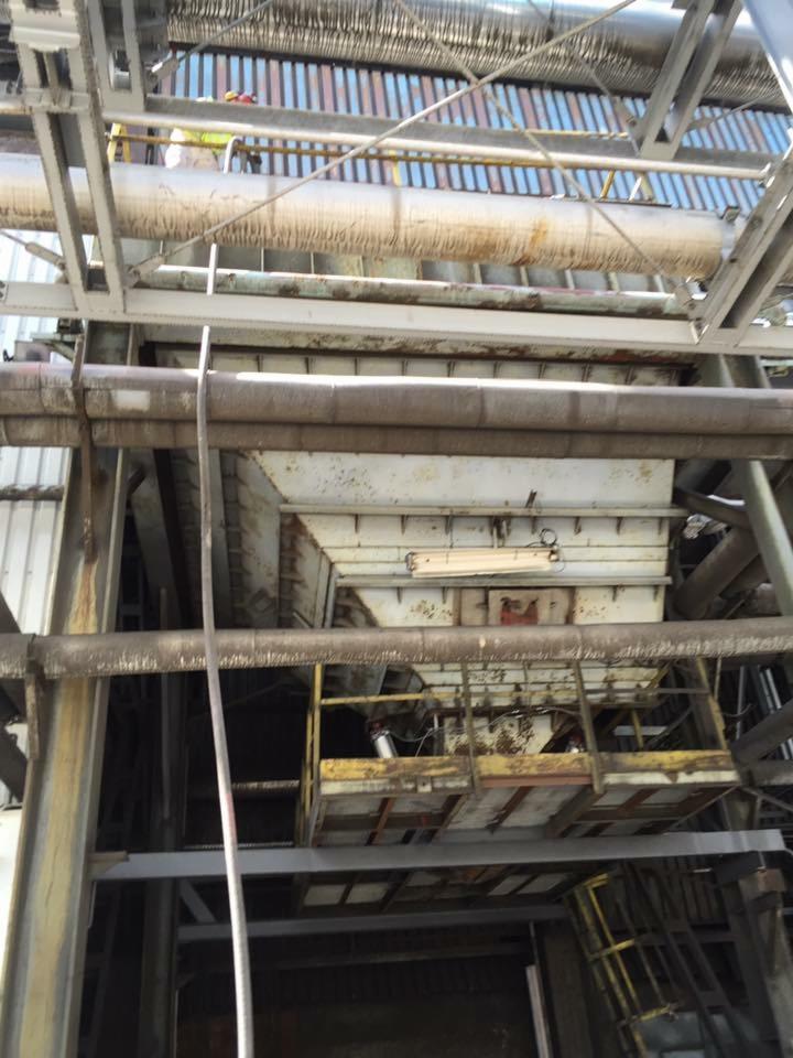 Wnętrze konstrukcji przemysłowej z metalowymi rurami i platformą roboczą, widoczne ślady korozji i zabrudzenia, oświetlenie górne