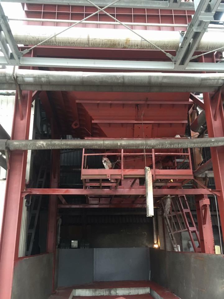 Wnętrze przemysłowej kabiny lakierniczej z czerwonymi elementami konstrukcyjnymi i widocznym pracownikiem na platformie roboczej.