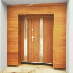 Wejście do domu z drewnianą ramą i drzwiami z przeszkleniami, wykończone poziomymi panelami w ciepłym odcieniu drewna.