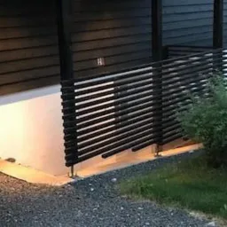 Nowoczesny, czarny taras z poziomymi deskami, oświetlony od dołu, z widocznym fragmentem trawnika i krzewu z boku.