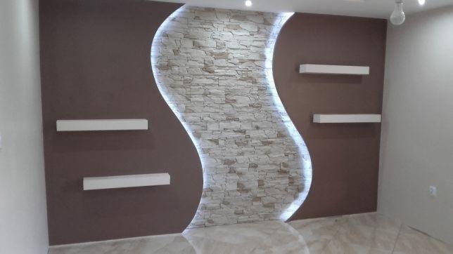 Brązowa ściana z dekoracyjnym, podświetlanym panelem z kamienia w kształcie litery S oraz trzema białymi półkami