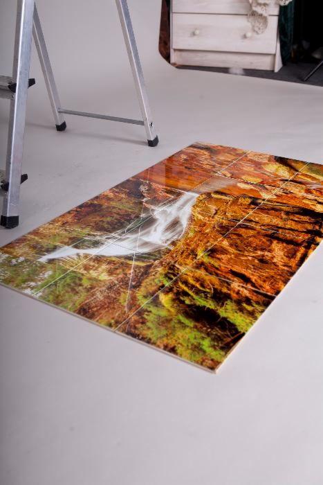 Ułożone płytki podłogowe z nadrukiem wodospadu, widoczne z bliska, w tle drabina i komoda.