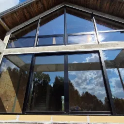 Nowoczesne okna z czarnymi ramami w domu o nietypowej architekturze, betonowe elementy konstrukcyjne, widok z dołu, odbicie nieba w szybach.