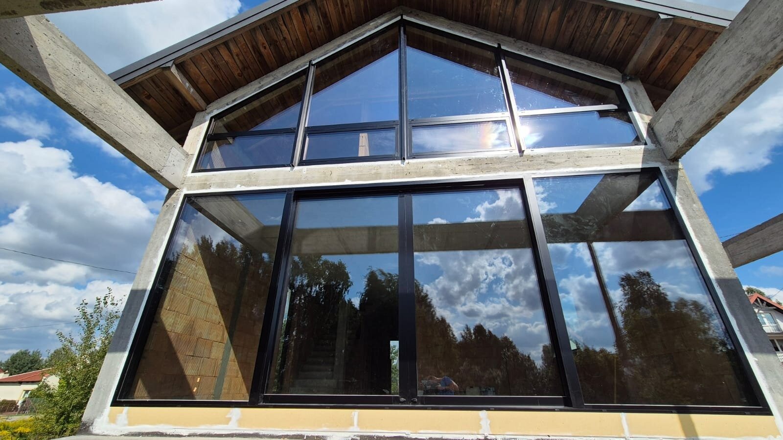 Nowoczesne okna z czarnymi ramami w domu o nietypowej architekturze, betonowe elementy konstrukcyjne, widok z dołu, odbicie nieba w szybach.