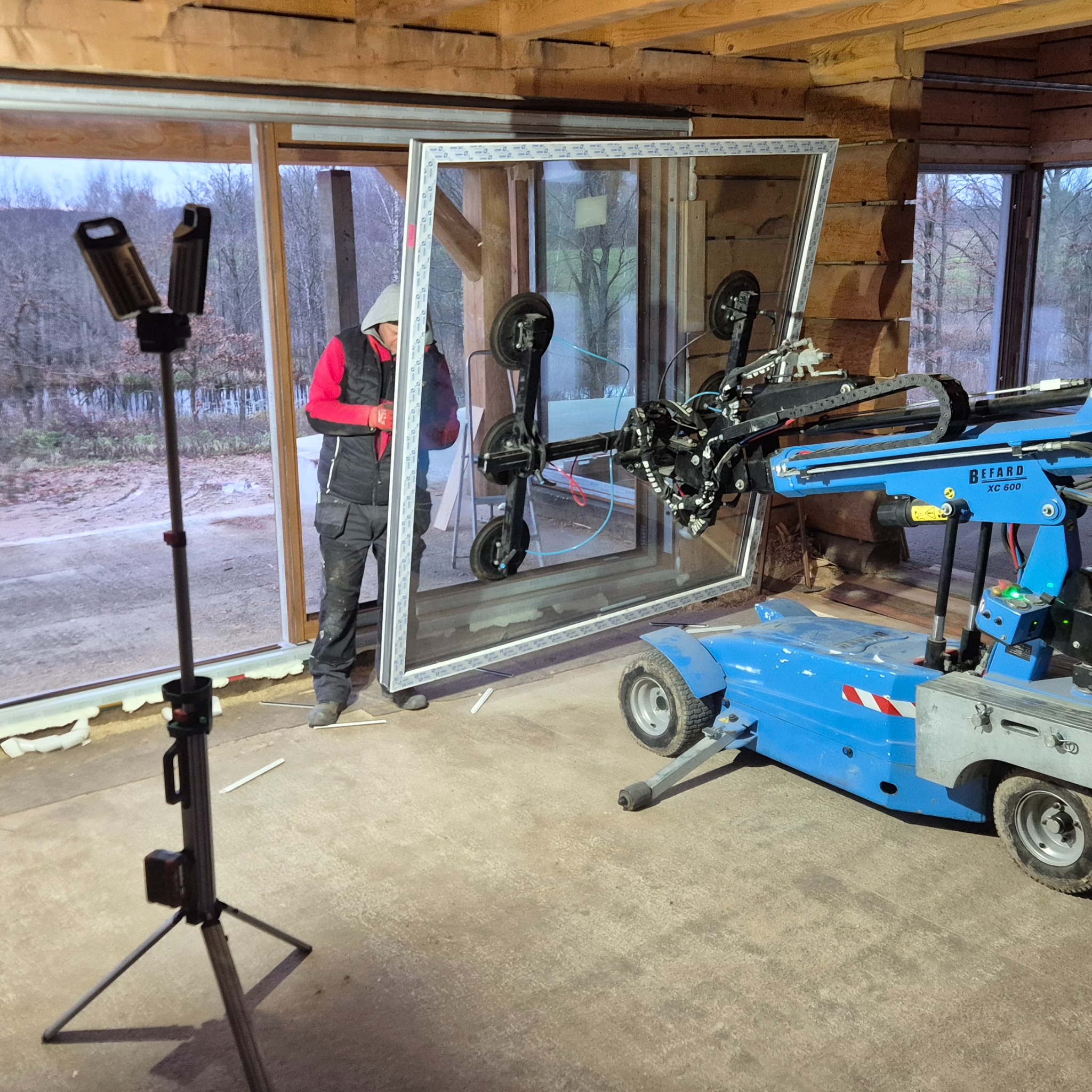 Montaż okna z użyciem specjalistycznego podnośnika Befard XC 600. Pracownik w odzieży roboczej nadzoruje proces. Widoczne narzędzia i elementy konstrukcyjne.