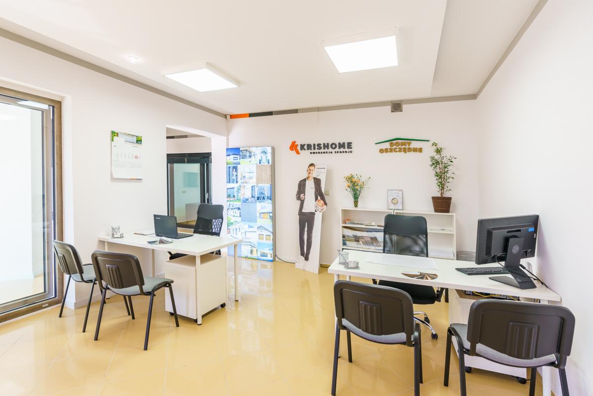 Jasne biuro sprzedaży stolarki okiennej i drzwiowej z ekspozycją okna PCV i materiałów reklamowych firm Krishome i Domy Oszczędne.