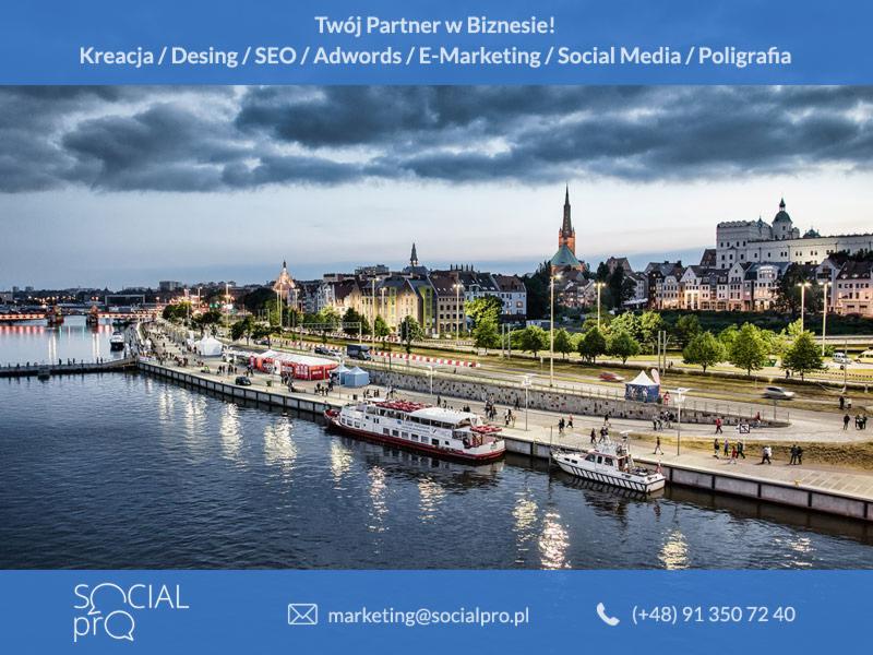 Panorama miasta nad rzeką z nabrzeżem, łodziami i hasłem reklamowym firmy oferującej usługi marketingowe i kreatywne.