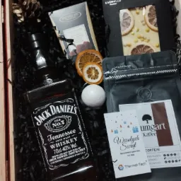 Zestaw prezentowy w drewnianej skrzynce, zawierający butelkę whisky Jack Daniel's, czekoladę Karmello z plastrami pomarańczy, trufla, kawę Umgart, bombkę kąpielową oraz suszone plastry pomarańczy...