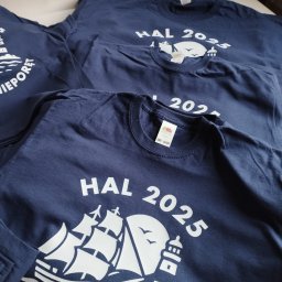 Endi-Mar Sp. z o.o. - Granatowe koszulki z białym nadrukiem: żaglowiec, latarnia morska i napis HAL 2025. Ułożone jedna na drugiej, widoczne metki. Detaliczny widok na gotowe produkty.
