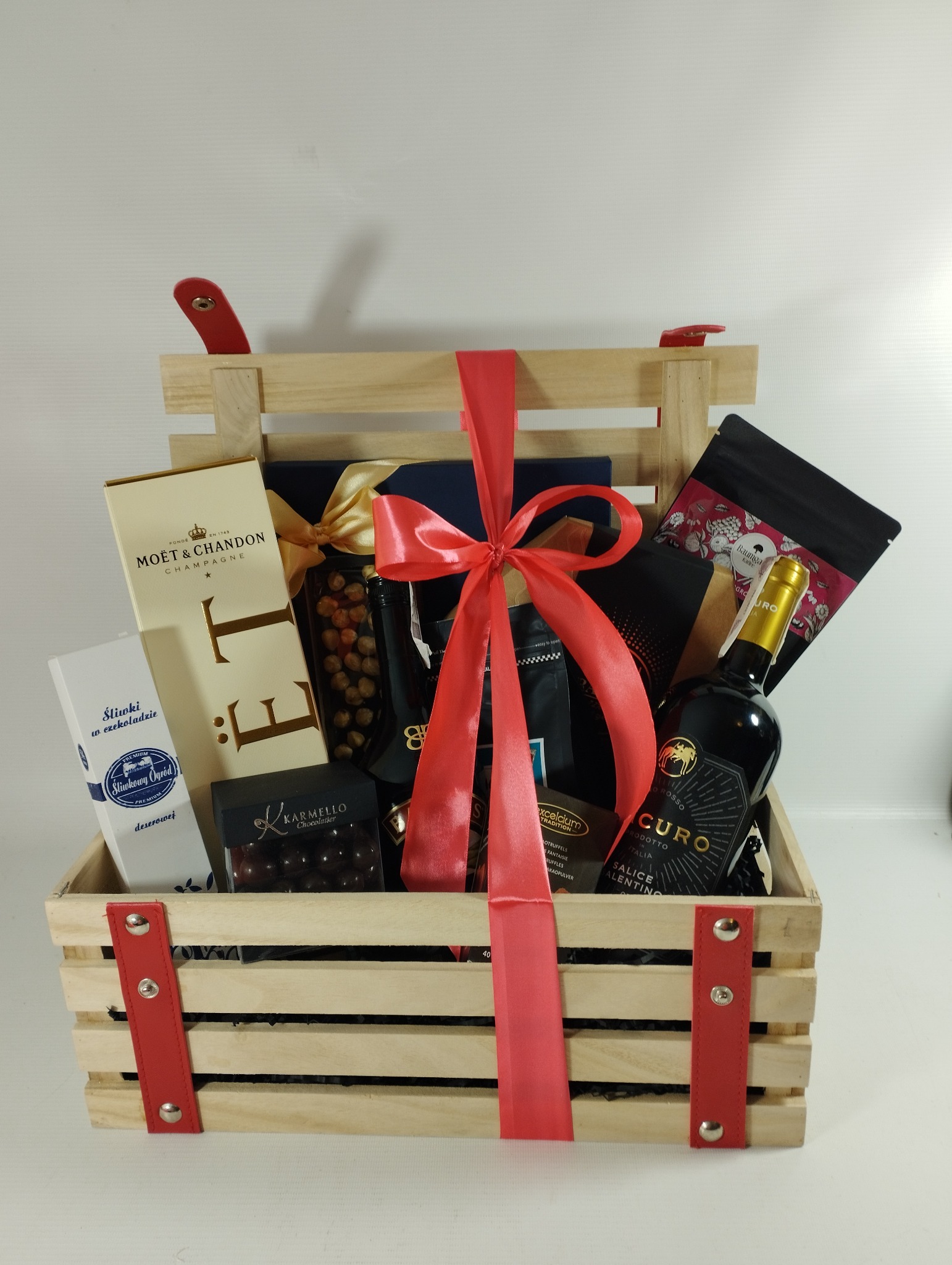Drewniana skrzynka prezentowa wypełniona luksusowymi produktami: szampan Moët & Chandon, czekoladki Karmello, śliwki w czekoladzie, orzechy laskowe w słoiku, butelka wina Curo Salice Salentino...