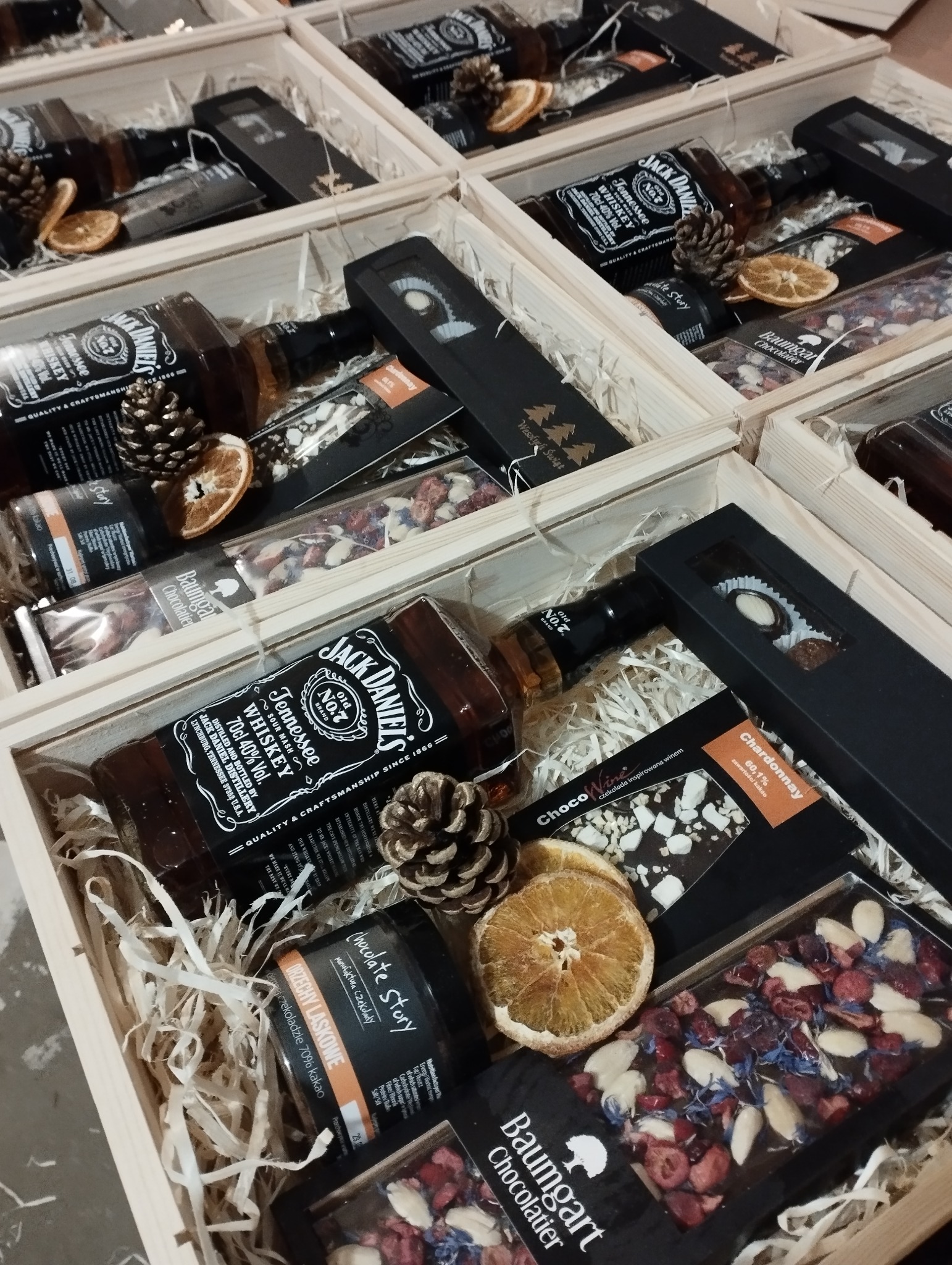 Drewniane skrzynki wypełnione prezentami: butelka Jack Daniel's, czekolady z owocami i orzechami Baumgart Chocolatier, słoik z orzechami laskowymi w czekoladzie Chocolate Story, suszone pomarańcze...