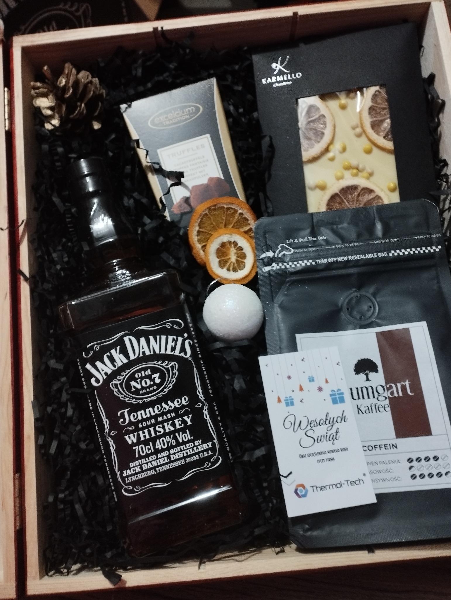 Zestaw prezentowy w drewnianej skrzynce, zawierający butelkę whisky Jack Daniel's, czekoladę Karmello z plastrami pomarańczy, trufla, kawę Umgart, bombkę kąpielową oraz suszone plastry pomarańczy...