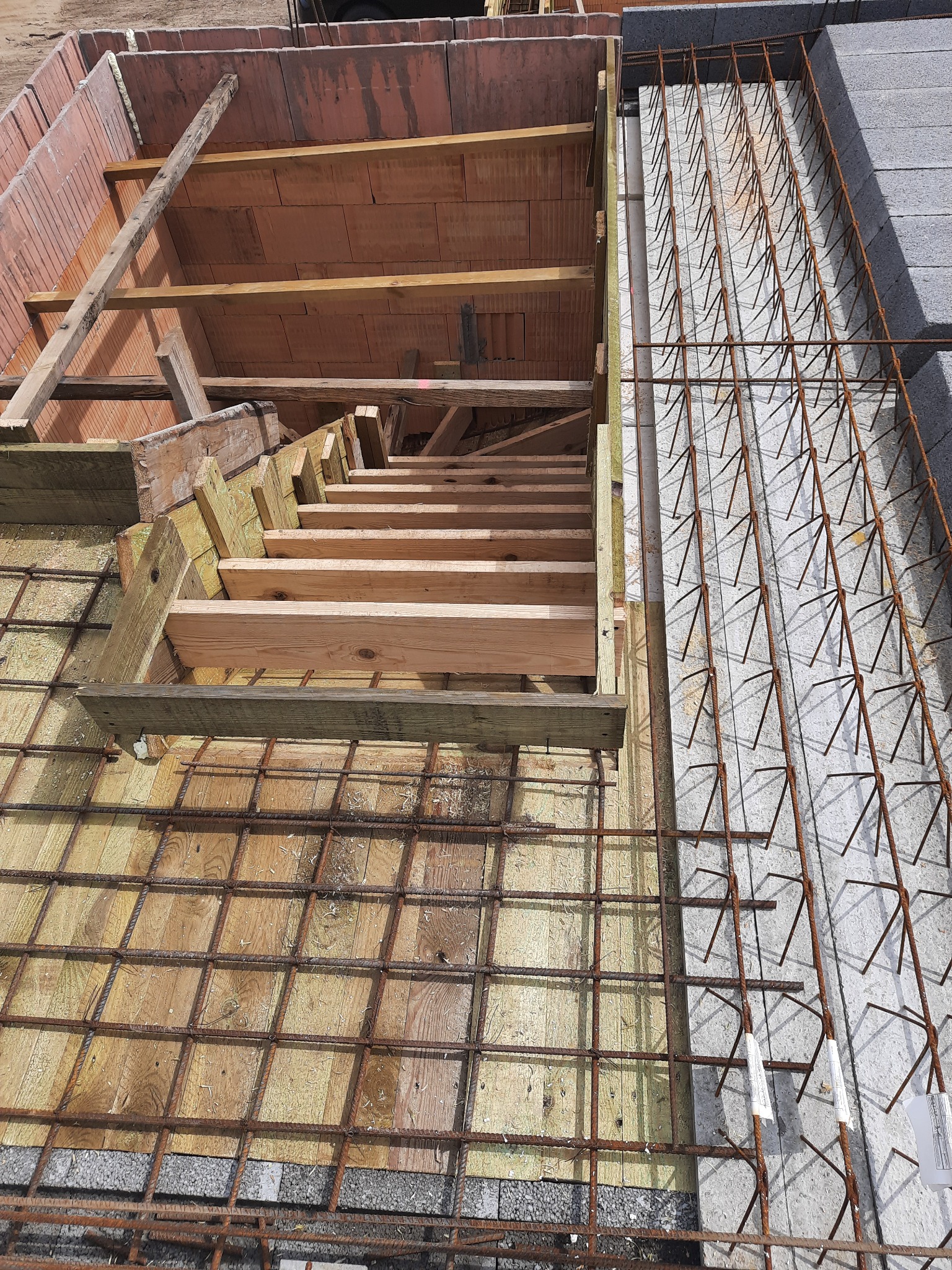 Wiązanie zbrojenia na drewnianym szalunku w trakcie budowy domu z bloczków ceramicznych i betonu komórkowego.