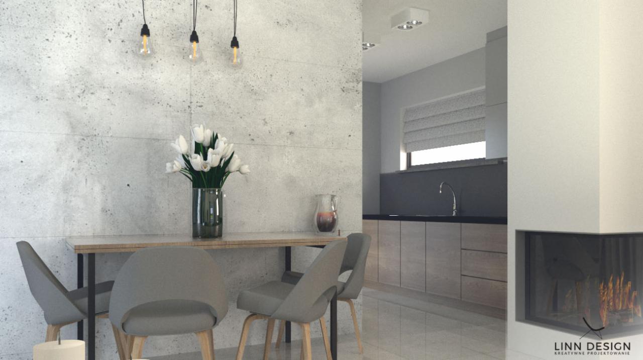 Jadalnia w nowoczesnym stylu z betonową ścianą, drewnianym stołem, szarymi krzesłami i bukietem białych tulipanów w szklanym wazonie, z widokiem na kuchnię w tle i kominek z boku