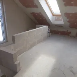 Ścianka działowa z bloczków z betonu komórkowego w surowym stanie, widoczne ślady po szpachlowaniu na skośnym suficie poddasza z oknami dachowymi.