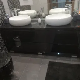 Nowoczesna łazienka z czarnymi meblami, dwiema białymi umywalkami nablatowymi, mozaikową ścianą i podświetleniem szafki.