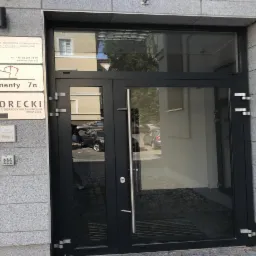 Wejście do budynku z szyldami: Kancelaria Radców Prawnych, Apartamenty 7a oraz Kancelaria Doradcy Finansowego Skorecki Spółka z o.o.