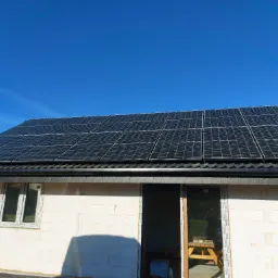 Dom w trakcie budowy z zamontowanymi panelami słonecznymi na dachu, widok z dołu na błękitne niebo.