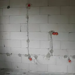 Surowe ściany z betonu komórkowego z widocznymi puszkami instalacyjnymi i przewodami elektrycznymi, częściowo zamurowane, przygotowane do dalszych prac wykończeniowych.