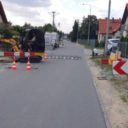 Instalacjekompleksowo.pl - Event Plus - Żółta minikoparka JCB z operatorem na ulicy w trakcie prac ziemnych przyłącza, widoczne zabezpieczenia i robotnicy.