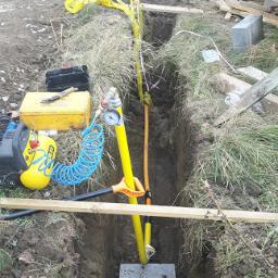 Instalacjekompleksowo.pl - Event Plus - Wykop z ułożoną rurą gazową na betonowej podstawie, zabezpieczoną żółtą taśmą ostrzegawczą, widoczny kompresor i narzędzia.
