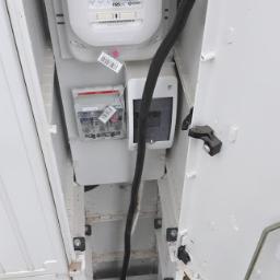 Instalacjekompleksowo.pl - Event Plus - Otwarta skrzynka elektryczna z licznikiem i przewodami, widok od góry, instalacja w trakcie podłączenia.