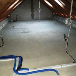 Instalacjekompleksowo.pl - Event Plus - Poddasze w trakcie instalacji: widoczne przewody elektryczne i rury hydrauliczne w niebieskiej karbowanej osłonie, prowadzone po podłodze. Surowy stan wykończenia, drewniana więźba dachowa.