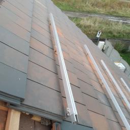 Instalacjekompleksowo.pl - Event Plus - Montaż szyn montażowych na dachówce ceramicznej przygotowanych pod instalację paneli fotowoltaicznych, widoczna osoba w oddali.