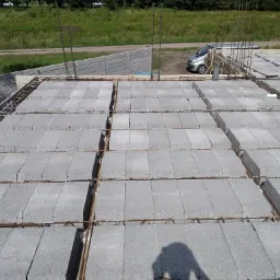 Wieniec stropowy Teriva zbrojony stalą, widoczne pustaki szalunkowe i wystające pręty zbrojeniowe, w tle zaparkowany samochód osobowy.