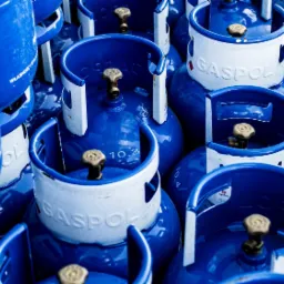 Stos niebieskich butli z gazem marki Gaspol, z białymi kołnierzami i zaworami, ustawionych blisko siebie, widoczne napisy i oznaczenia na butlach.